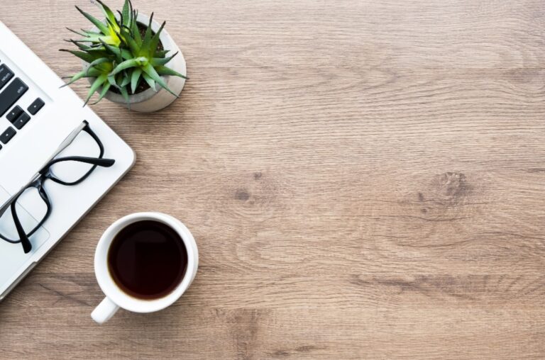 Eine Ecke vom Laptop sichtbar mit einr Brille darauf. Eine Kaffeetasse steht davor.